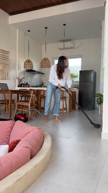 A woman vacuums the floor in a modern, open-plan living area and kitchen.