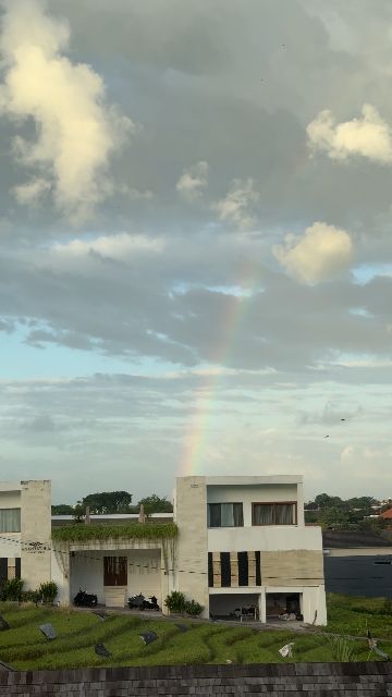 A rainbow stretches across a cloudy sky above modern buildings with green roofs.
