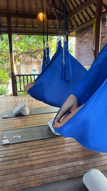 A person relaxes in a blue yoga hammock in a serene open-air studio.