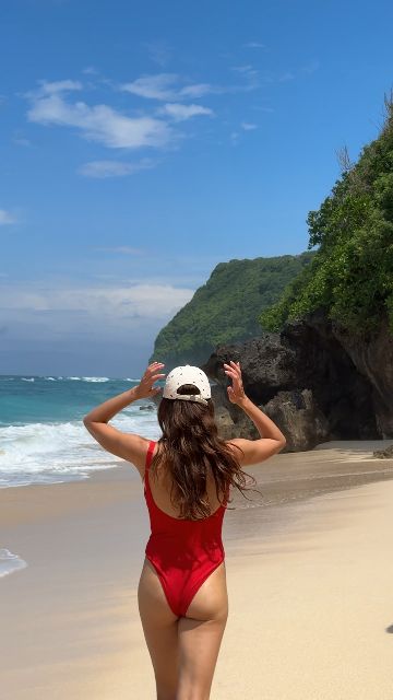 A woman in a red swimsuit plays joyfully in the ocean waves on a sunny beach.